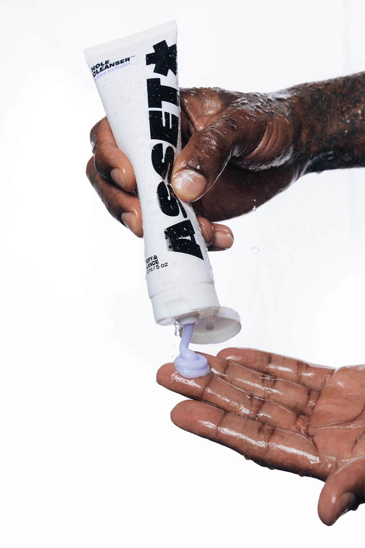 A close-up of a person squeezing a white tube labeled Asset Hole Cleanser onto their palm against a white background.