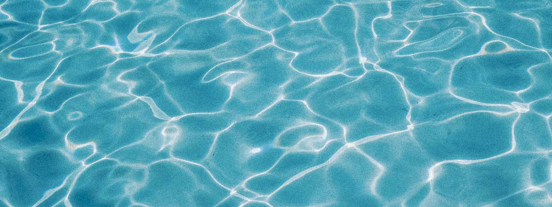 Clear turquoise pool water with bright white caustic light patterns rippling across the surface.