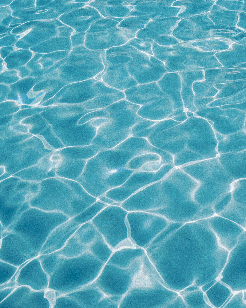 Clear turquoise pool water with bright white sunlight patterns reflecting across the surface.